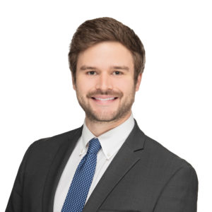 A man in a suit and tie is smiling against a plain white background.