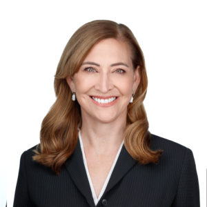 A woman with shoulder-length brown hair is smiling and wearing a dark blazer.