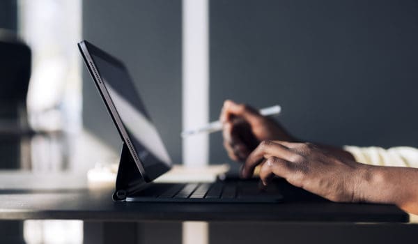 Unrecognizable African-American business woman typing notes on a keyboard while having online web conference on a digital tablet in a restaurant