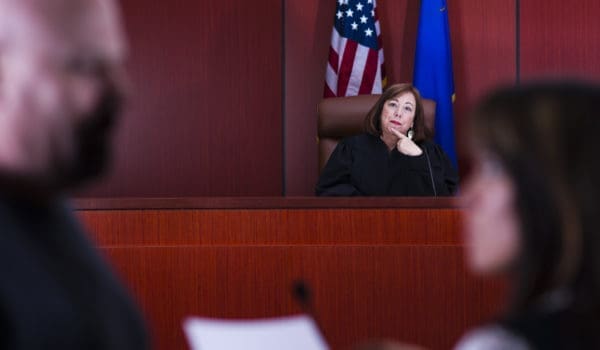 Stock photo of a judge in her sixties watching an attorney explain papers to a defendant.