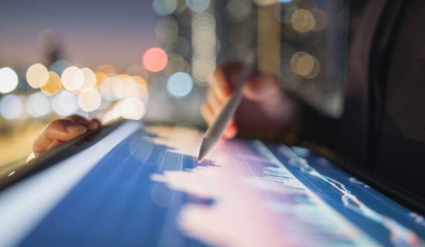 A close-up of a person using a digital tablet with a stylus to analyze financial data, representing consumer financial services. The glowing screen displays graphs and charts, symbolizing data-driven insights, regulatory compliance, and consumer protection in the evolving landscape of consumer finance.