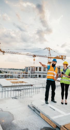 Employees working on construction site, wearing protective equipment and discussing next construction phase - full length models visible on the image