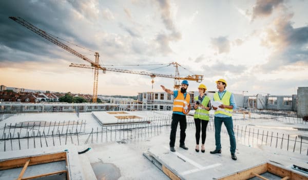 Employees working on construction site, wearing protective equipment and discussing next construction phase - full length models visible on the image