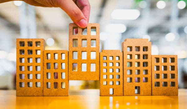 Hand choosing mini wood house model from model on wood table, selective focus, Planning to buy property. Choose what's the best. A symbol for construction ,ecology, loan concepts
