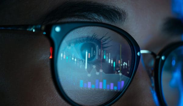 Female trader wearing eyeglasses with reflection of stock market charts