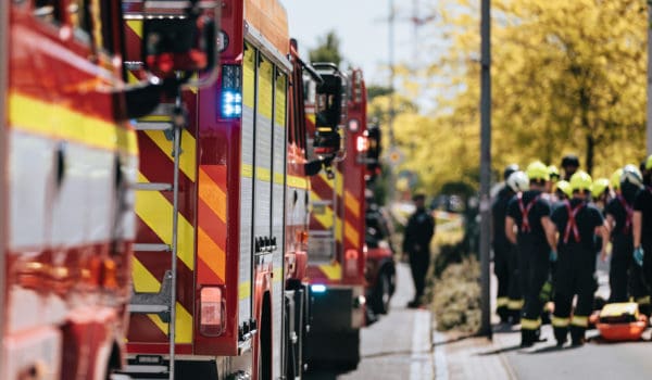Red fire trucks in row. Teams of fire brigade on city street. Selective on blue flasher.